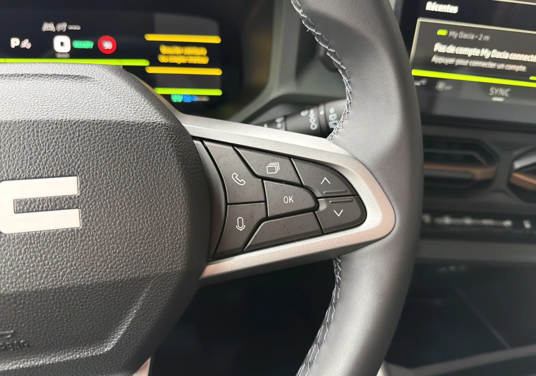 Gros plan sur la partie droite du volant noir du Dacia Bigster Hybrid 155 Extreme avec commandes intégrées et écran tactile en arrière-plan.