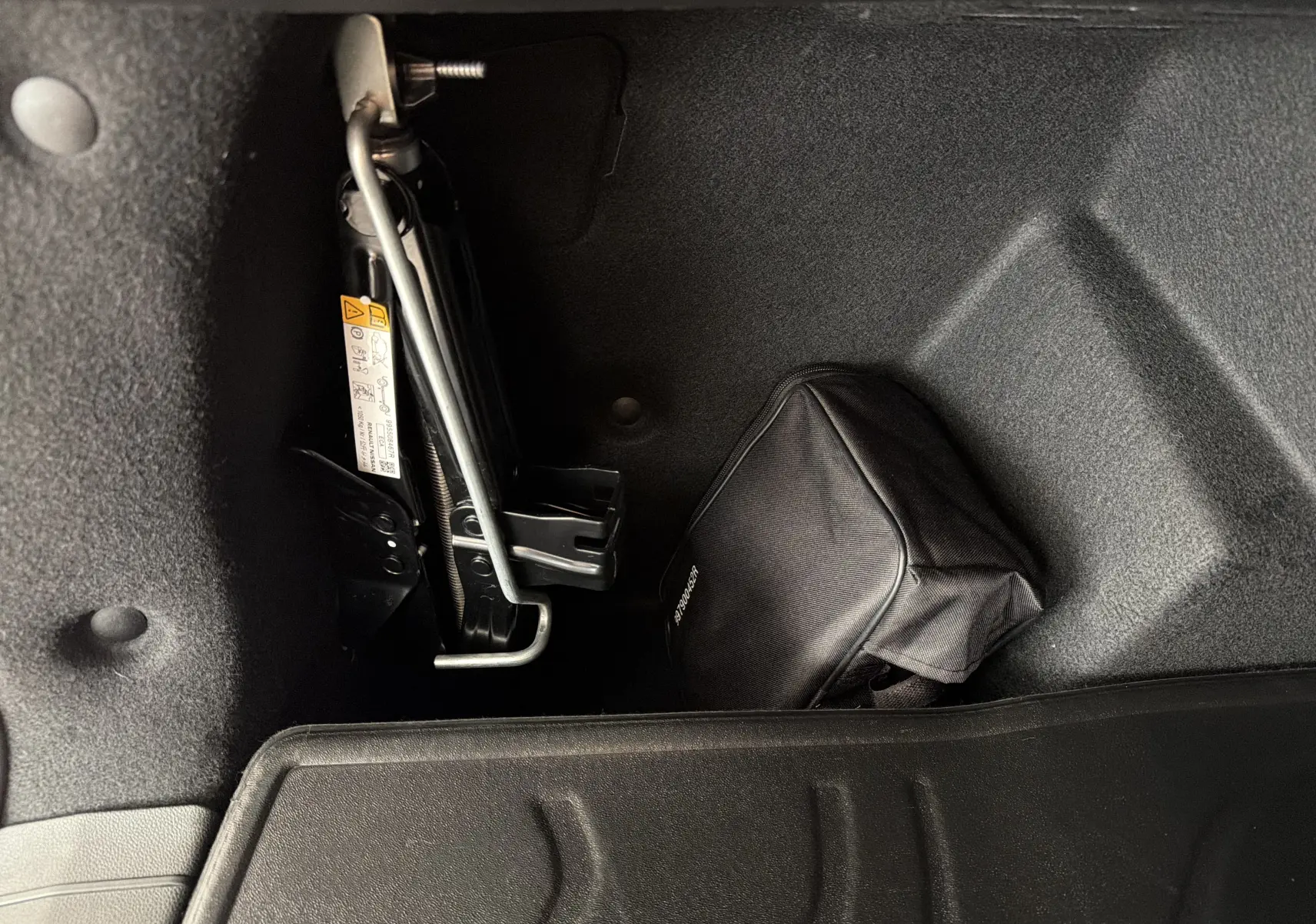Coffre du Dacia Bigster Hybrid 155 Extreme 2026, vue intérieure montrant le cric et une trousse noire de secours.
