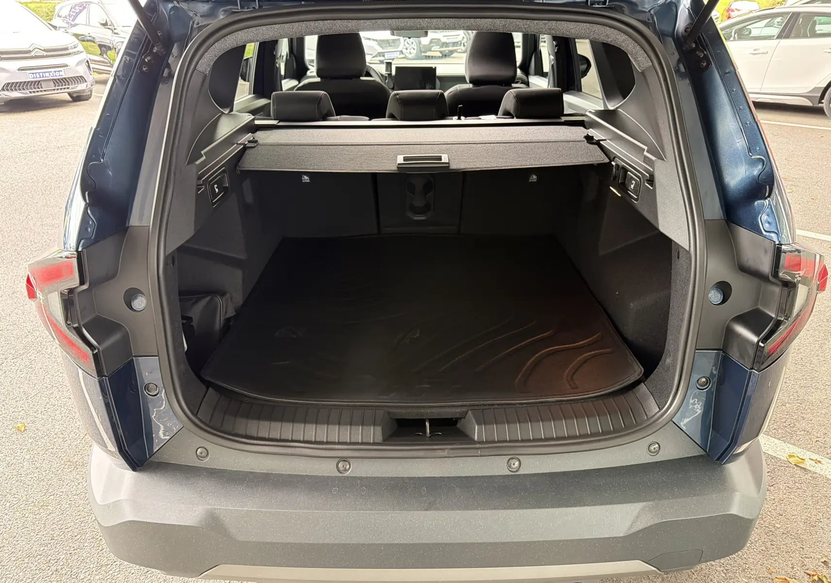 Vue arrière du coffre ouvert du Dacia Bigster Hybrid 155 Extreme bleu indigo, montrant l'espace de chargement et la plage arrière.