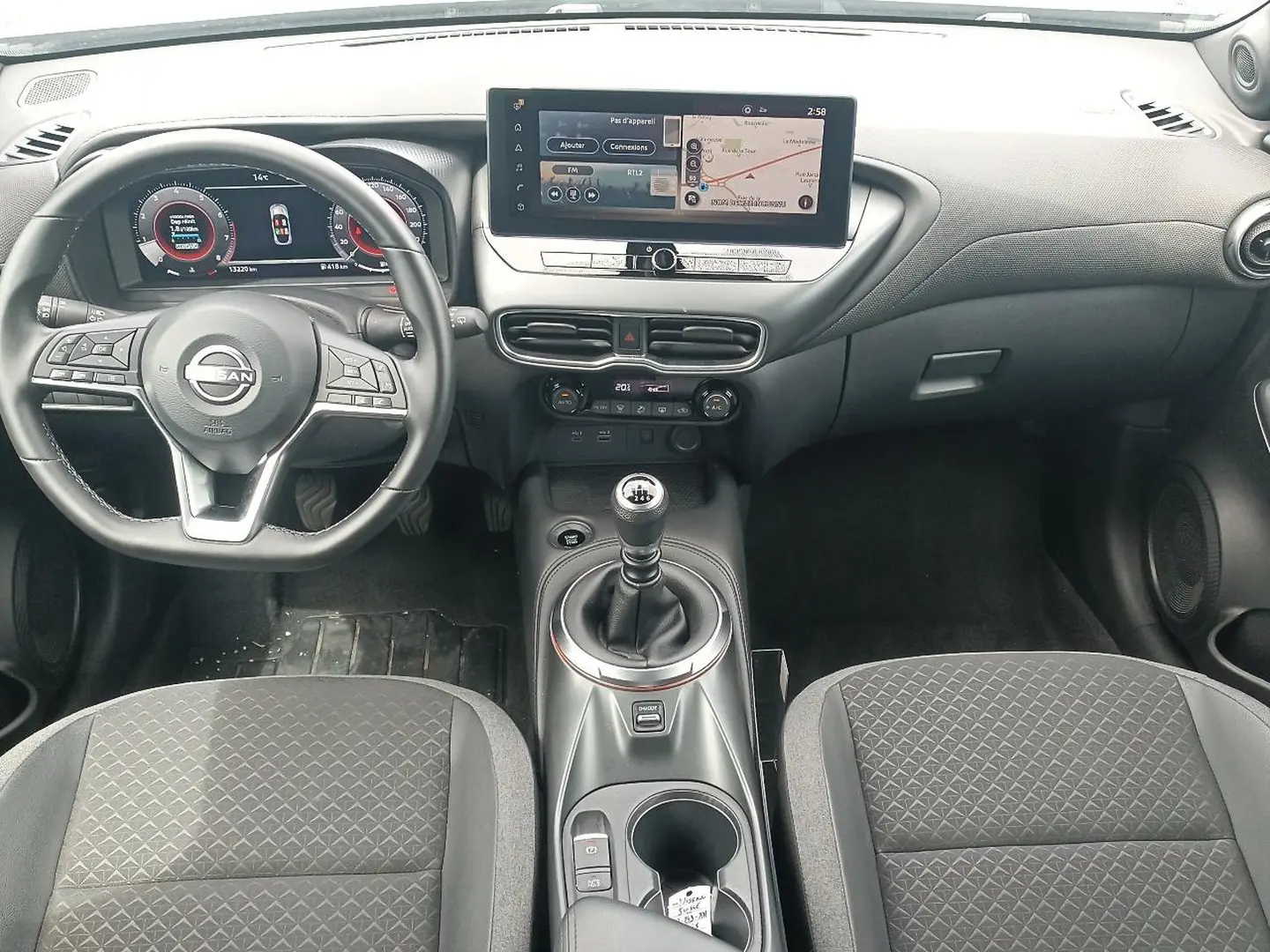 Vue intérieure avant du Nissan Juke 2025 avec tableau de bord numérique, écran tactile et levier de vitesse manuel.