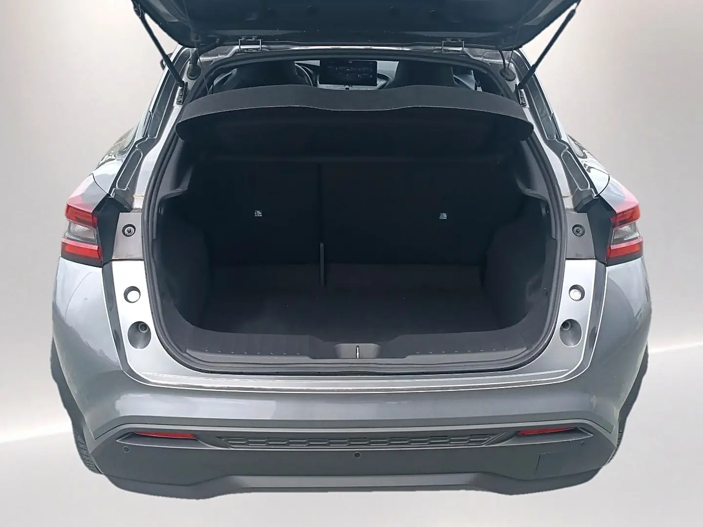 Vue arrière du coffre ouvert d'un Nissan Juke gris 2025, montrant l'espace de chargement vide et les feux arrière LED.