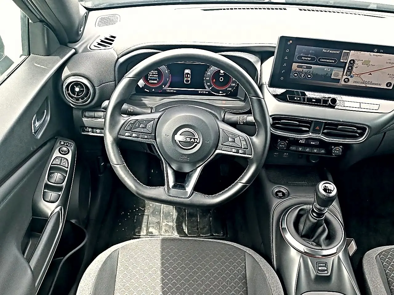 Vue intérieure centrée sur le volant cuir multifonction et la console avec boîte manuelle du Nissan Juke gris 2025.