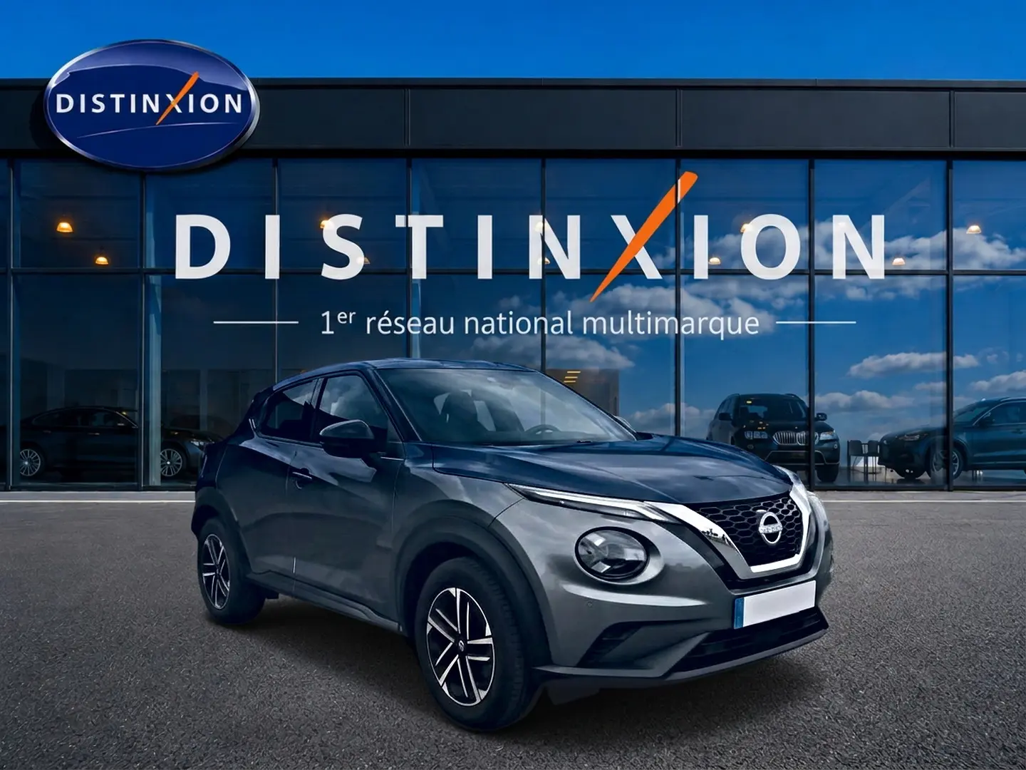Nissan Juke gris en 3/4 avant droit, avec calandre V-Motion chromée et jantes alliage noires.