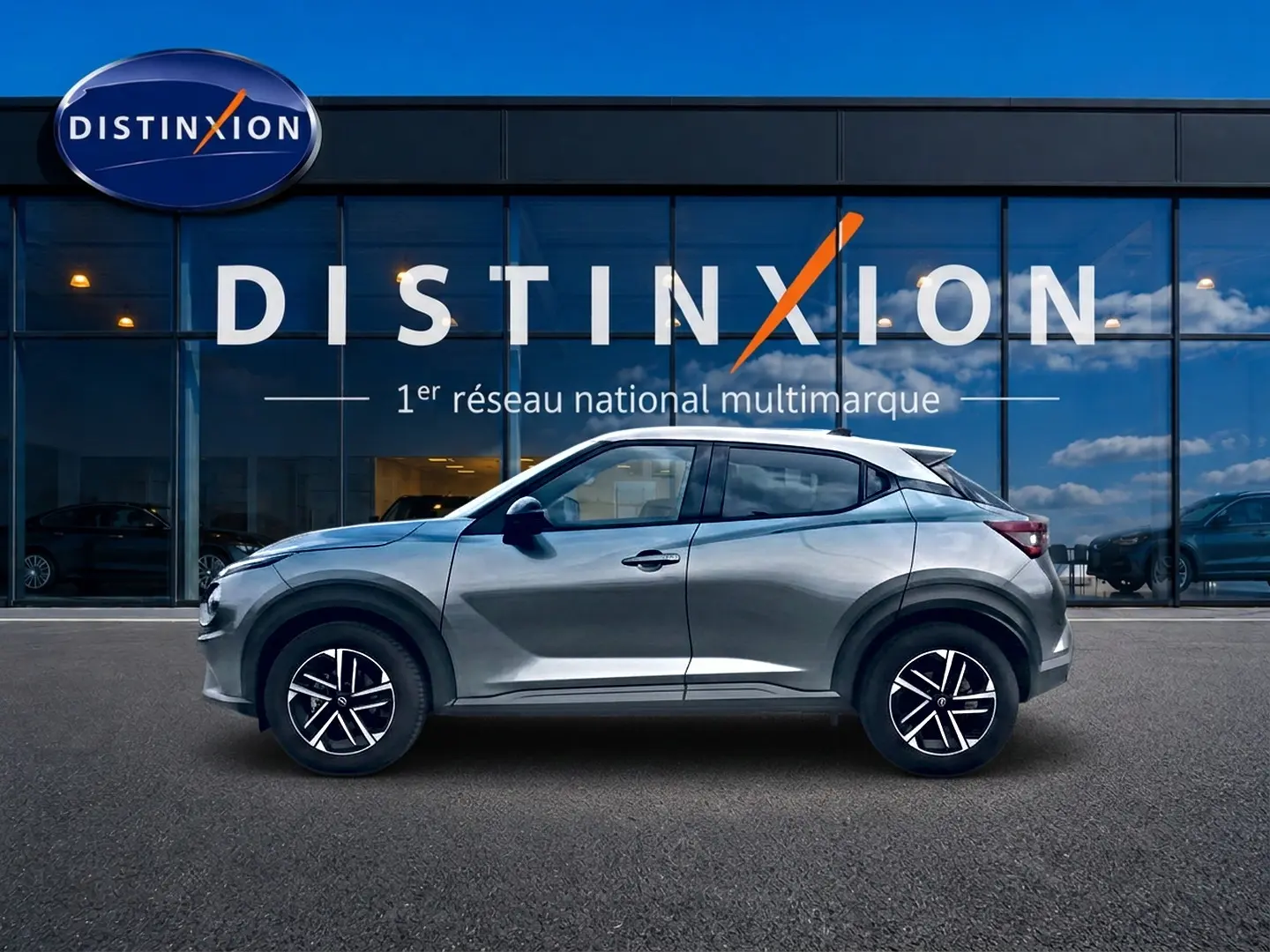 Nissan Juke gris vue de profil côté gauche, avec jantes alliage et toit blanc contrasté, devant une vitrine Distinxion.