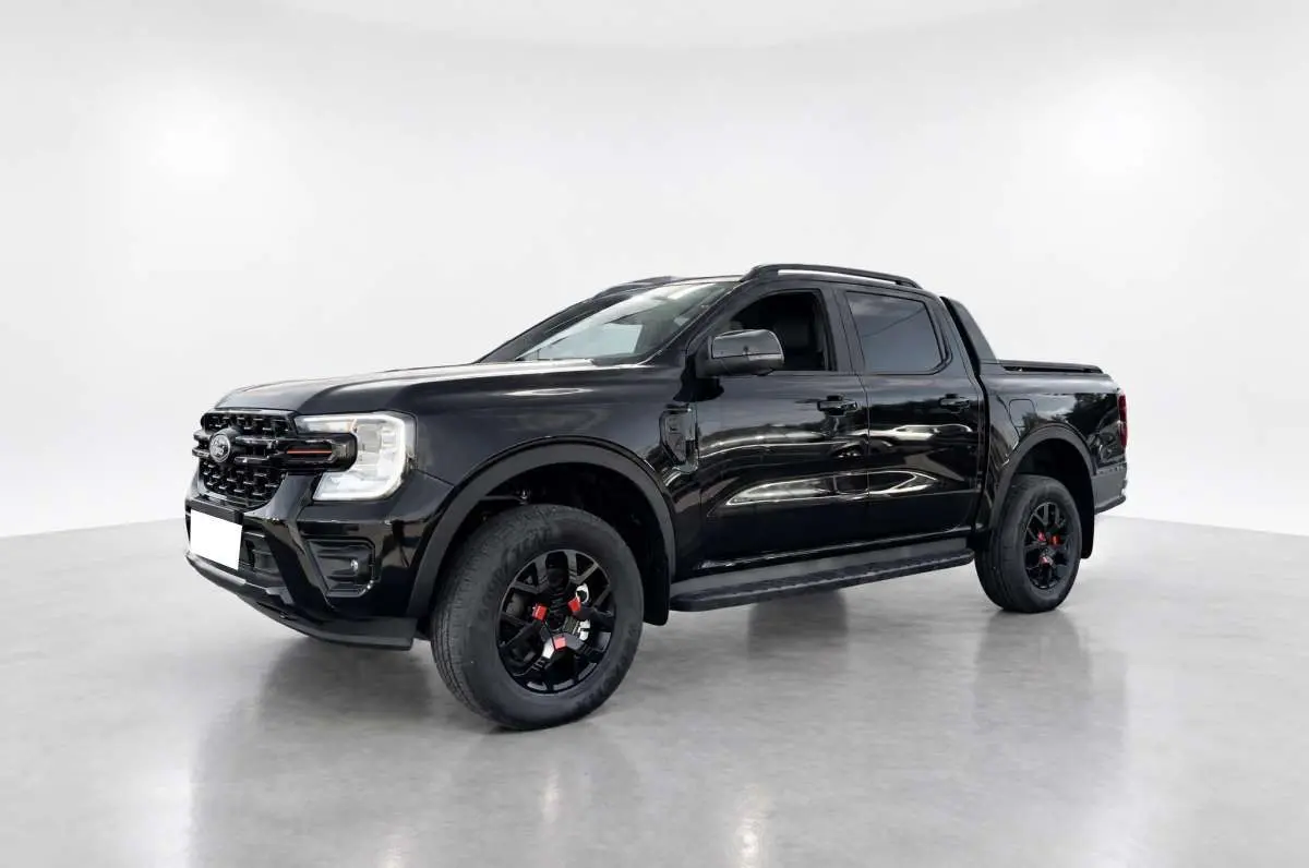 Ford Ranger Wildtrak Plus noir agate en 3/4 avant droit, avec jantes noires et barres de toit visibles.