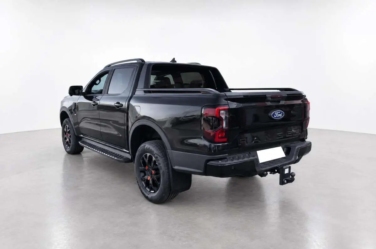 Ford Ranger Wildtrak noir agate vu en 3/4 arrière droit, avec attelage et jantes noires distinctives.