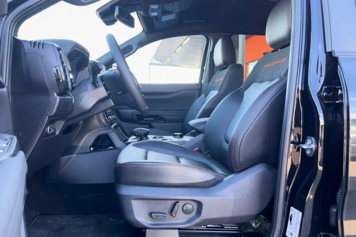 Vue côté conducteur intérieur du Ford Ranger Wildtrak 2026 noir agate, sièges cuir avec surpiqûres orange et logo Wildtrak.