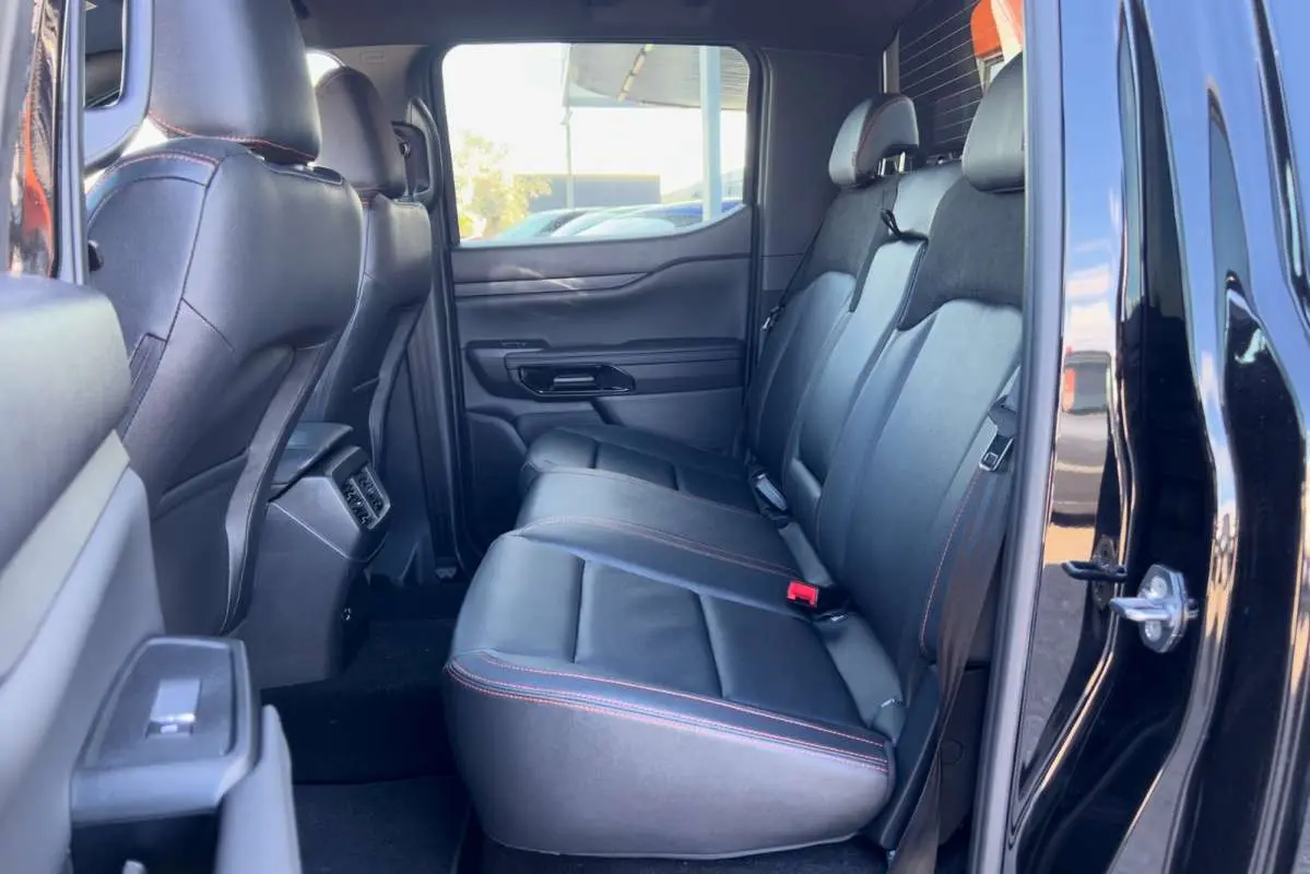 Vue intérieure arrière côté droit du Ford Ranger Wildtrak noir agate, montrant les sièges en cuir avec surpiqûres orange.
