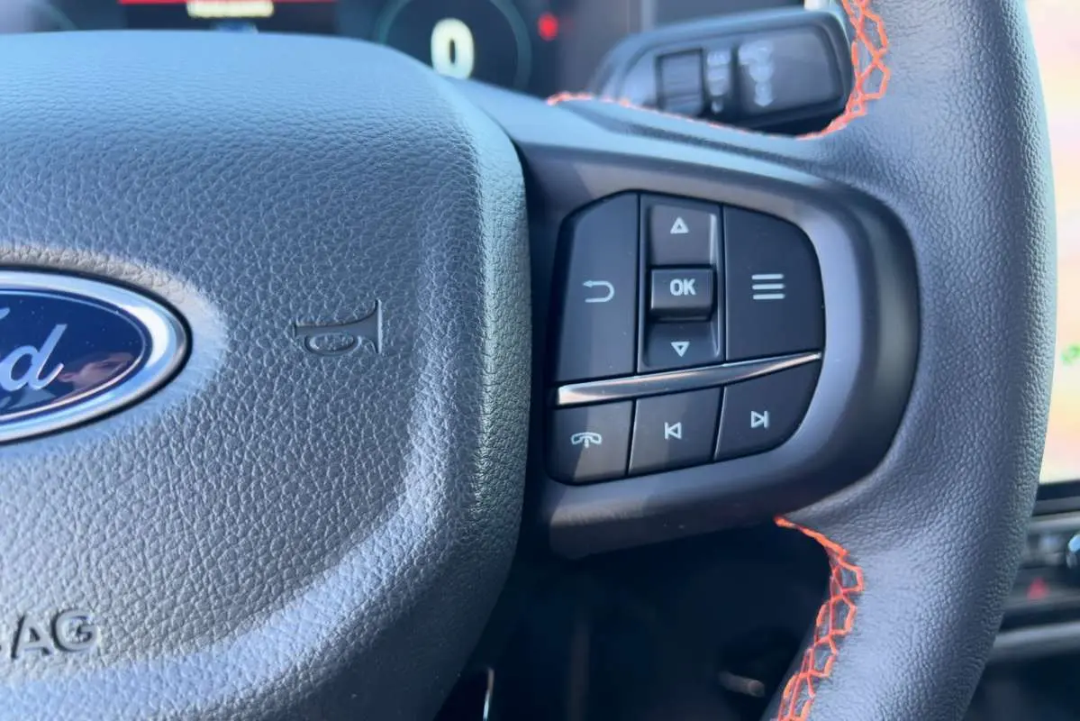 Gros plan sur le volant noir en cuir avec surpiqûres orange et commandes multifonctions du Ford Ranger 2026.