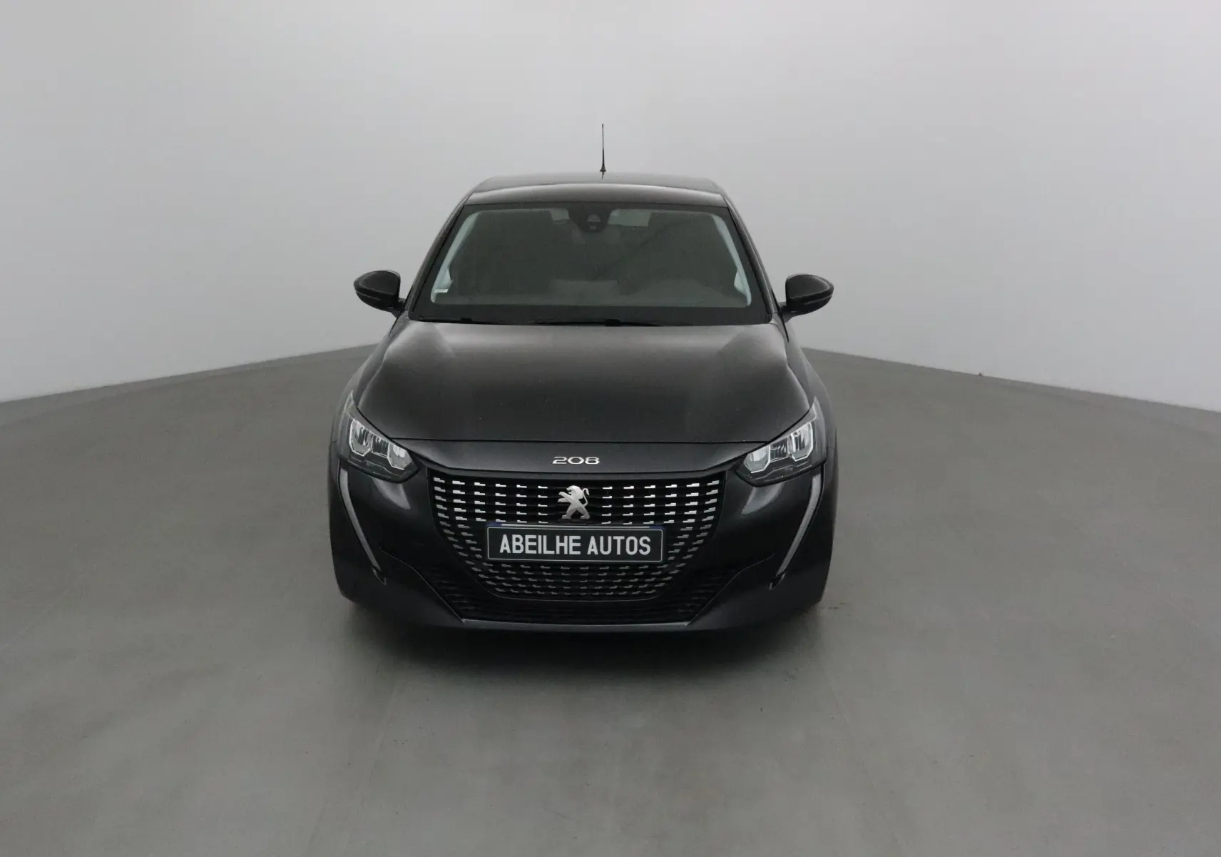 Peugeot 208 noire vue de face, mettant en valeur sa calandre distinctive et ses phares LED modernes.
