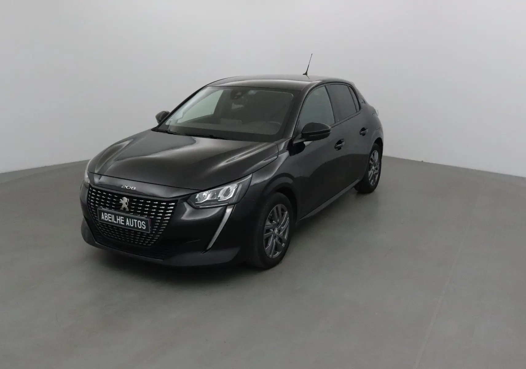 PEUGEOT 208 noir vue 3/4 avant droit dans un studio, calandre marquée et jantes alliage visibles.