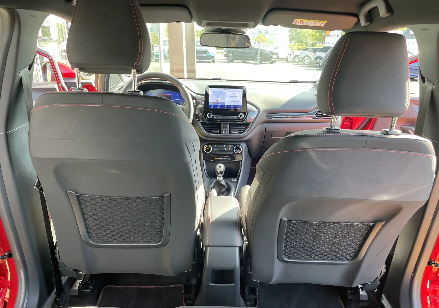 Vue intérieure arrière du Ford Puma rouge 2021, montrant les sièges avant noirs avec surpiqûres rouges et la console centrale avec écran tactile.