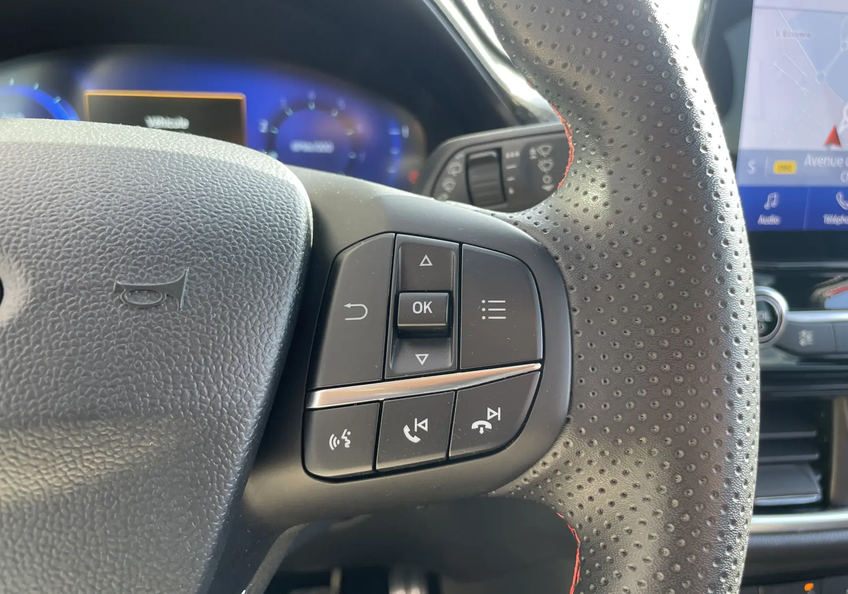 Gros plan sur les commandes multifonctions du volant perforé noir avec surpiqûres rouges du Ford Puma 2021.