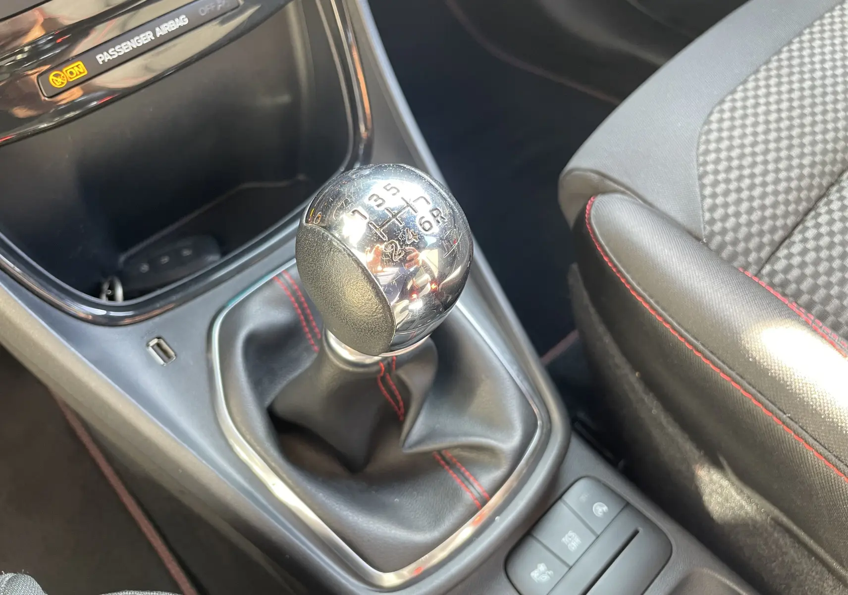 Gros plan sur le levier de vitesse manuel chromé et le siège tissu noir avec surpiqûres rouges dans le Ford Puma rouge 2021.