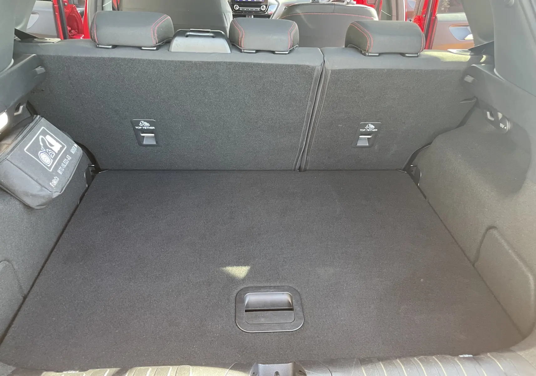 Coffre ouvert d'un Ford Puma rouge 2021, vue intérieure arrière montrant banquette arrière et espace de chargement noir.