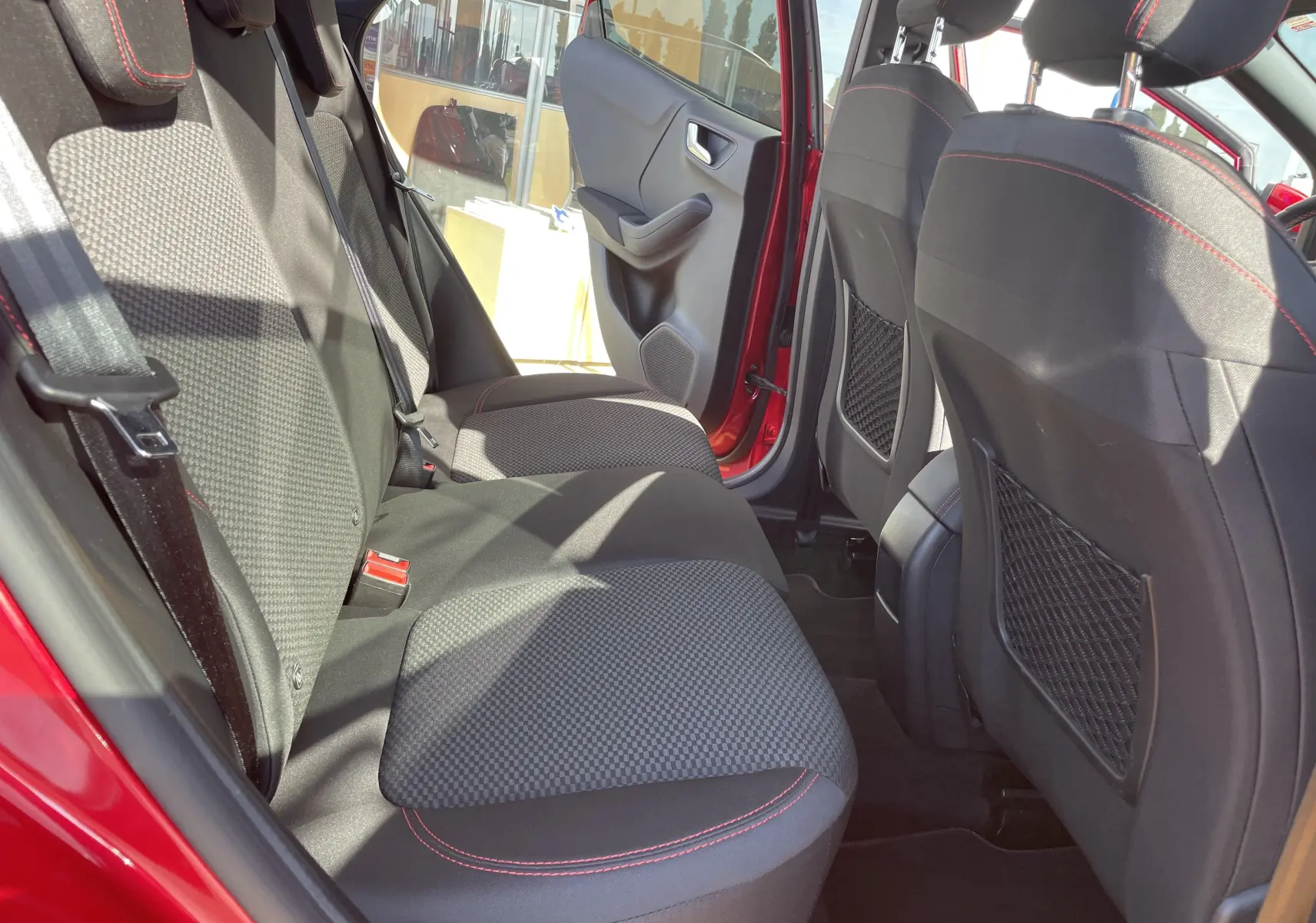 Vue intérieure arrière du Ford Puma rouge 2021, montrant les sièges arrière en tissu noir avec surpiqûres rouges et portières ouvertes.