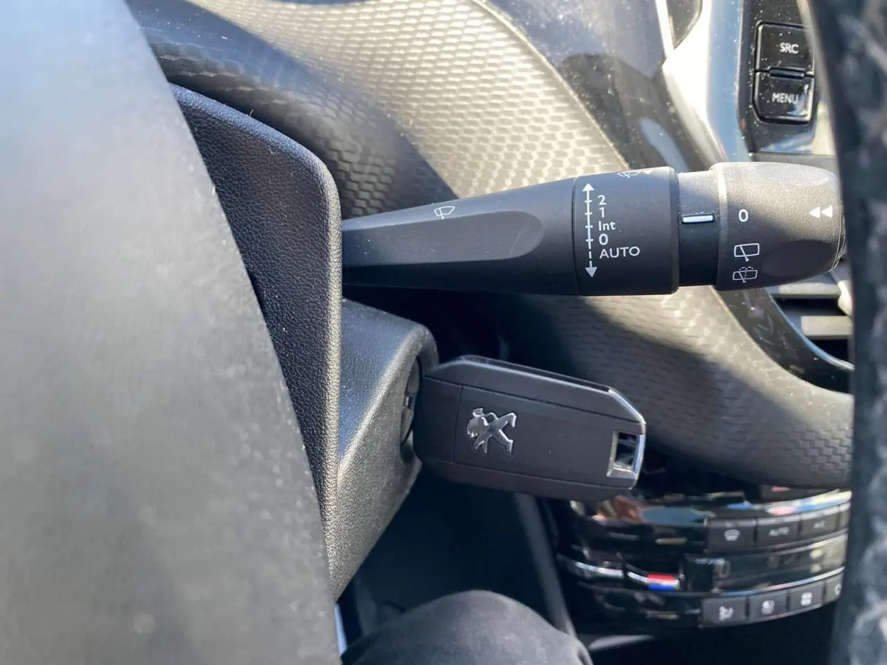 Gros plan sur la clé Peugeot insérée dans le contacteur, volant noir et commandes de lève-glace en arrière-plan.