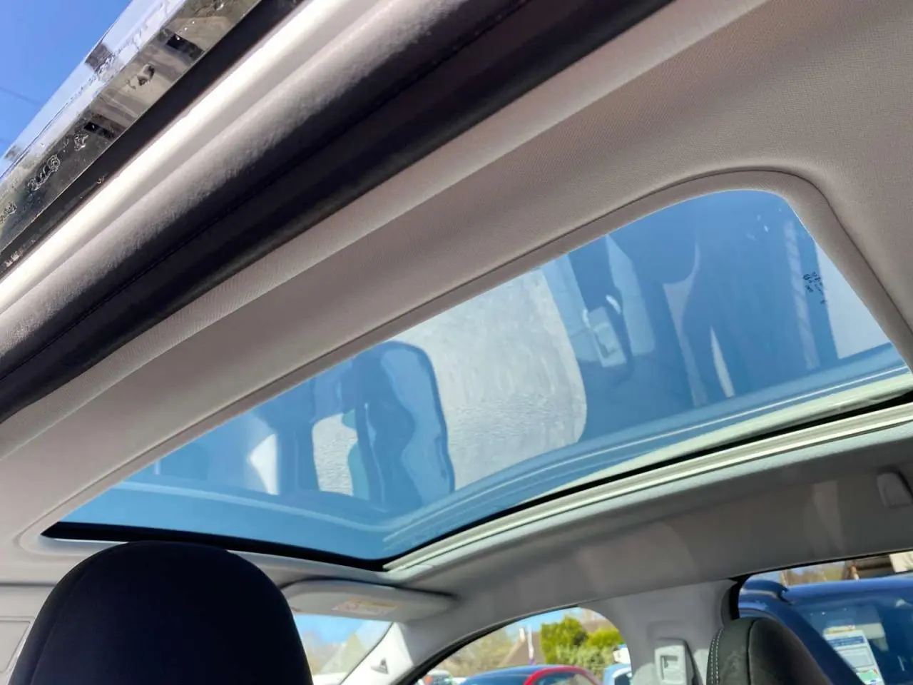 Toit vitré panoramique ouvert vu de l'intérieur arrière d'un Peugeot 2008 avec ciel bleu visible à travers le verre.