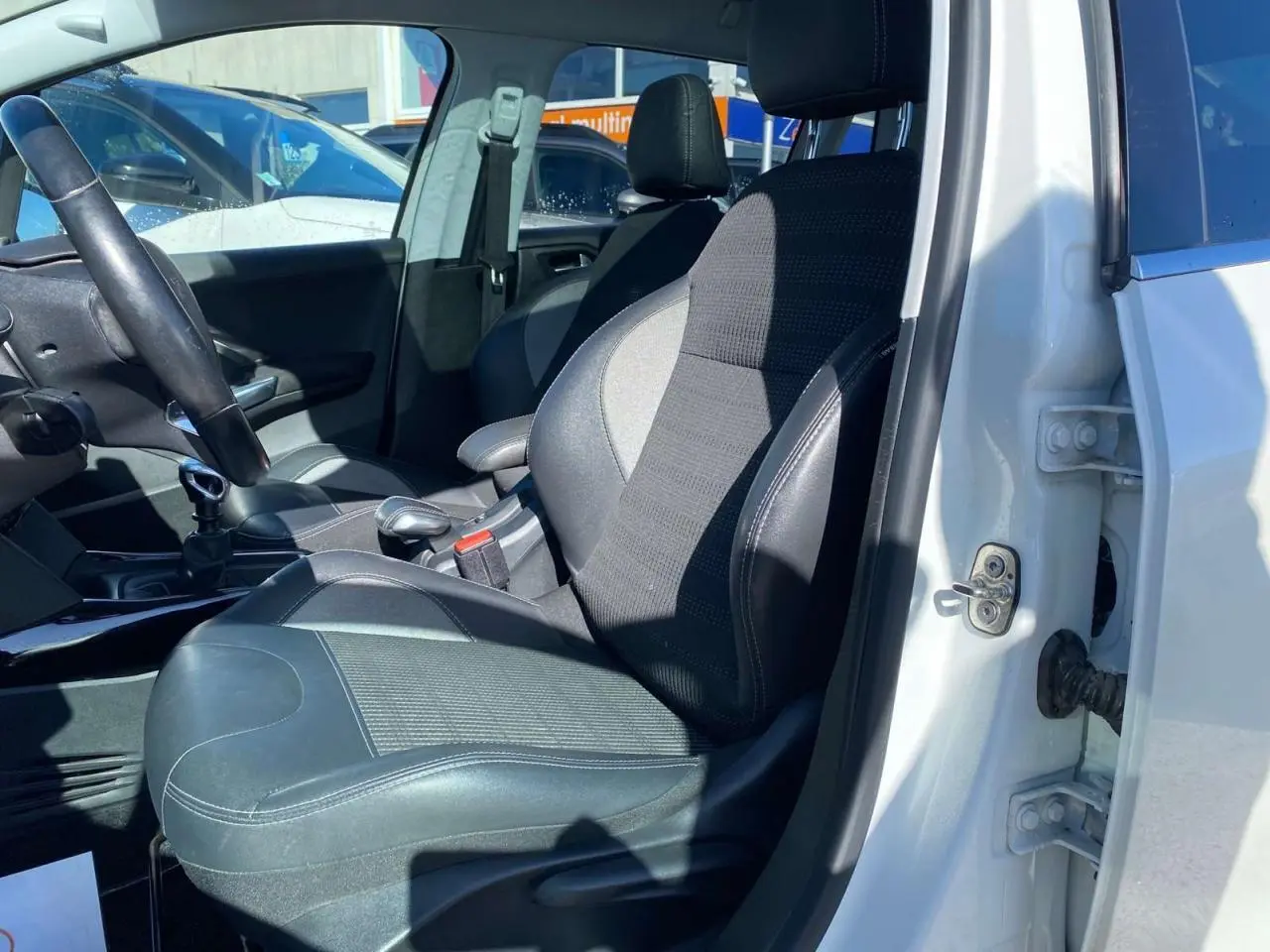 Vue intérieure côté conducteur d'une Peugeot 2008 blanche de 2019 avec siège en tissu et cuir noir.