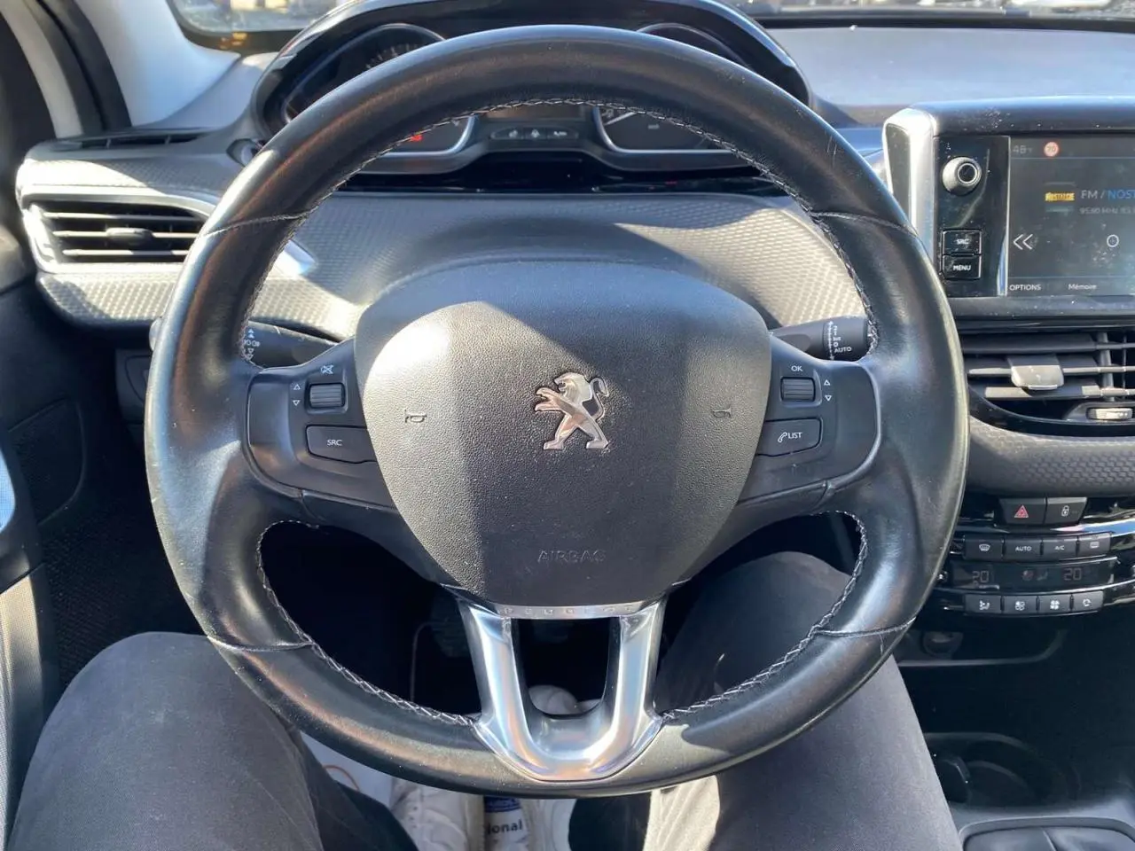 Vue rapprochée du volant cuir noir d'une Peugeot 2008 2019 avec tableau de bord et écran tactile multifonction.