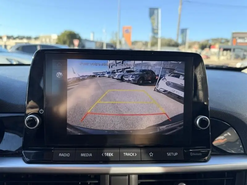 Écran de caméra de recul dans une KIA Picanto gris foncé 2023, vue arrière avec lignes de guidage colorées.