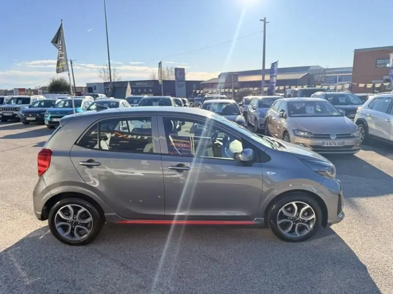 Vue de profil droit d'une KIA Picanto 2023 gris foncé GT Line avec jantes alliage et bande rouge distinctive sur bas de caisse.