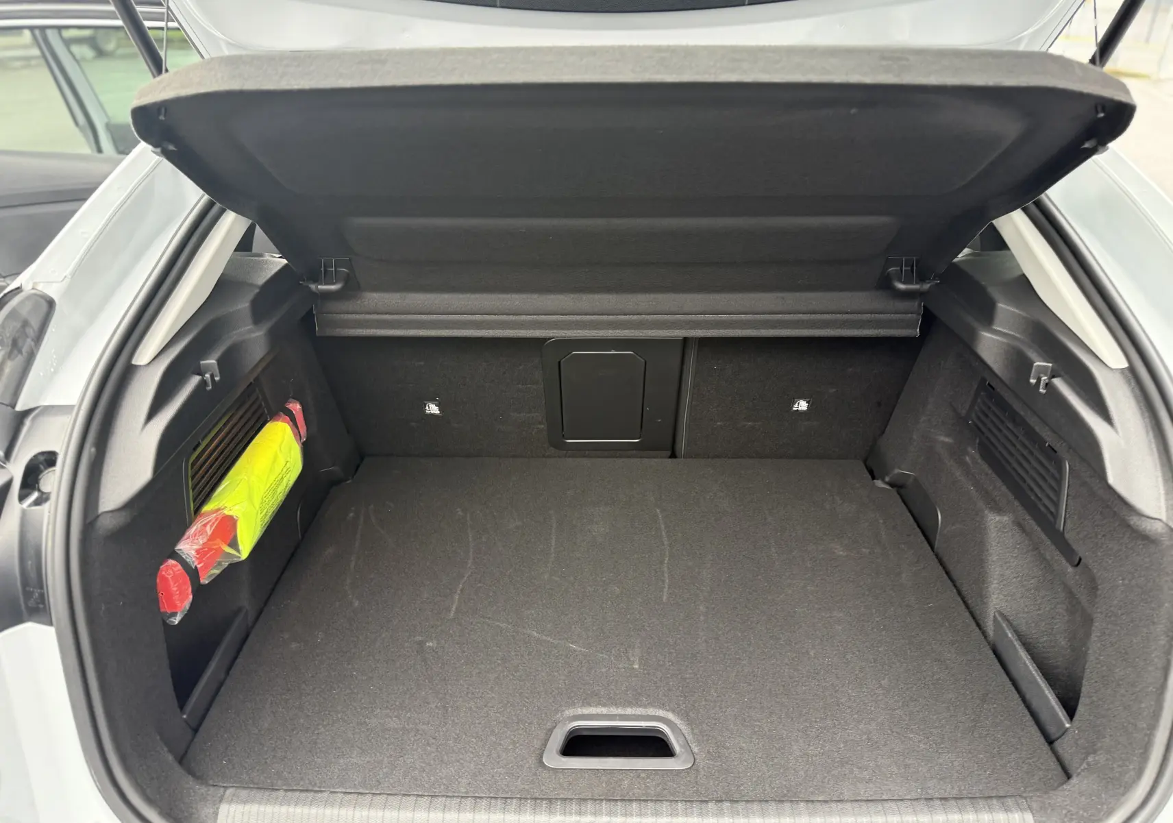 Coffre ouvert vu de l'arrière d'une Citroën C4 Hybrid 145 blanc Okenite, avec rangement noir et triangle de sécurité visible.