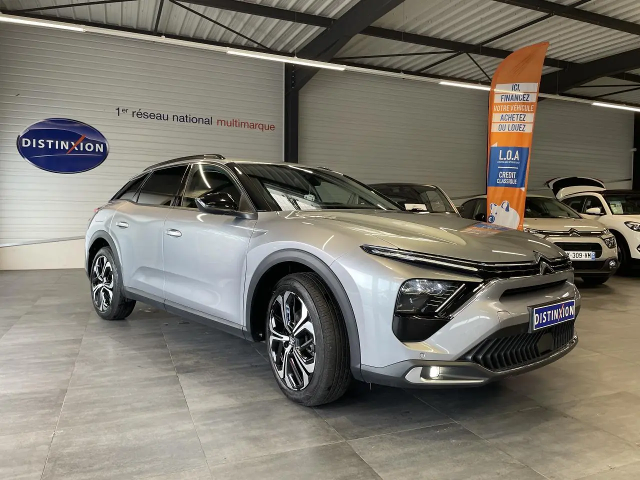 Vue 3/4 avant d'une Citroën C5 X 2024 gris foncé, avec jantes alliage et calandre distinctive dans un showroom.