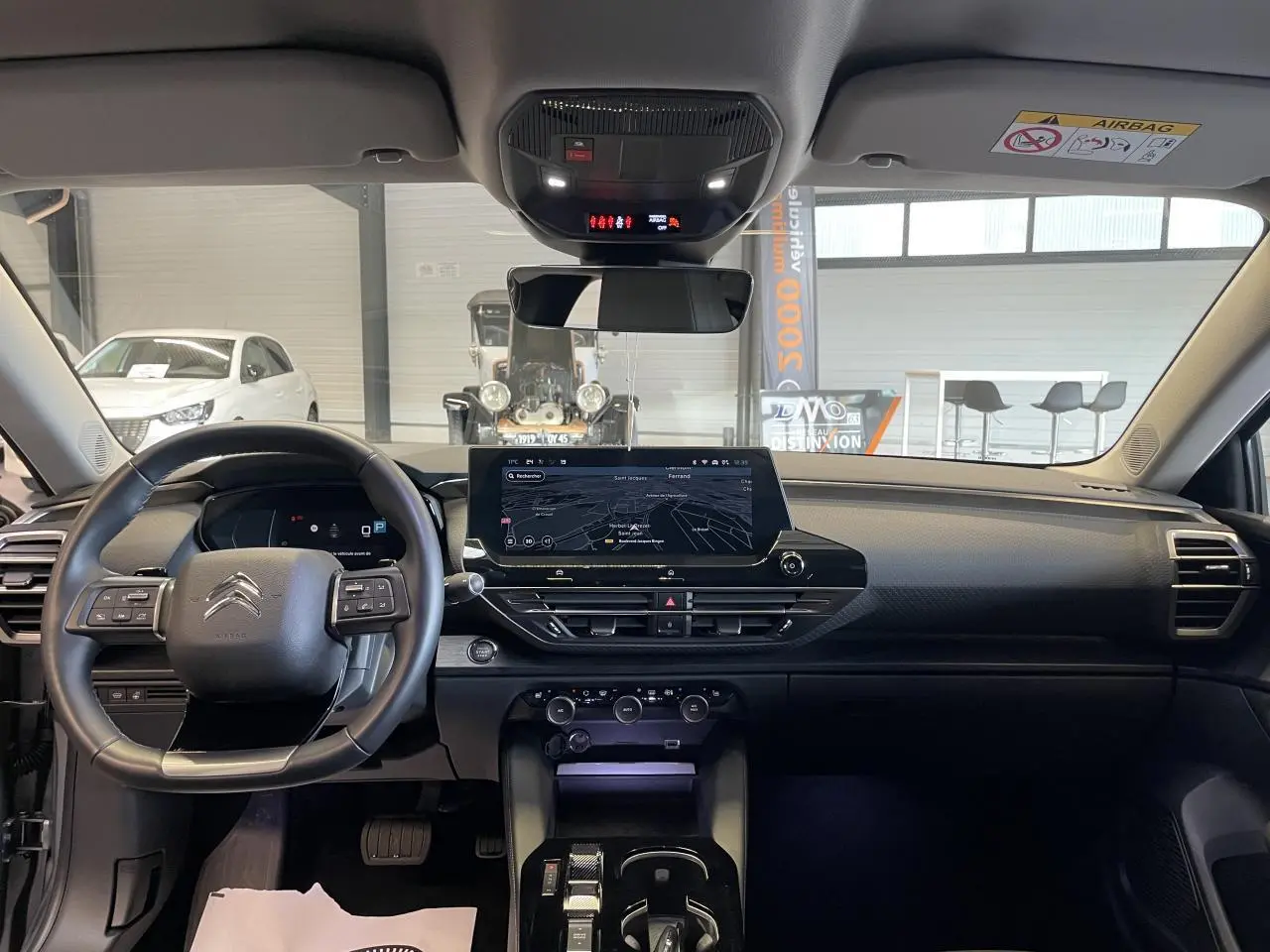 Vue intérieure frontale du tableau de bord noir de la Citroën C5 X 2024 avec écran tactile central et volant multifonction.