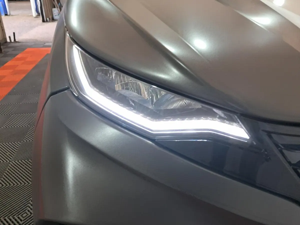 Gros plan sur le phare avant droit gris clair de l’Aixam Ambition 2024 avec éclairage LED distinctif allumé.