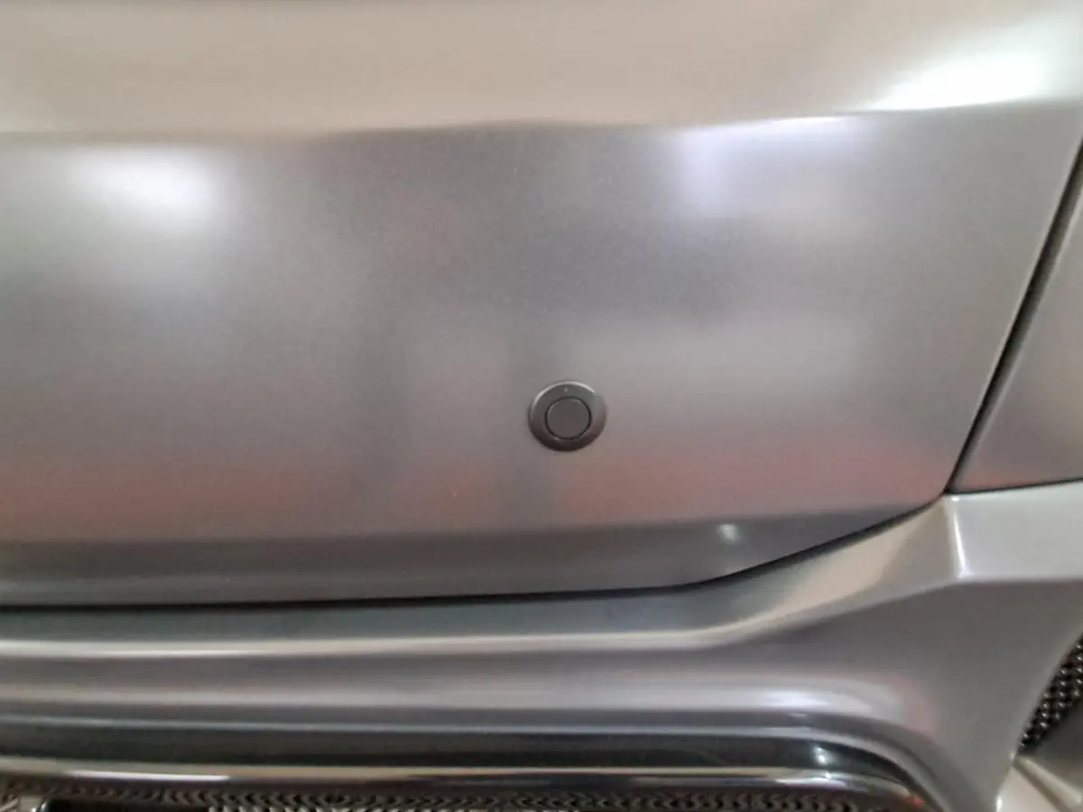 Gros plan sur le pare-chocs gris clair de l'Aixam Ambition 2024, mettant en valeur un capteur de radar de recul intégré.