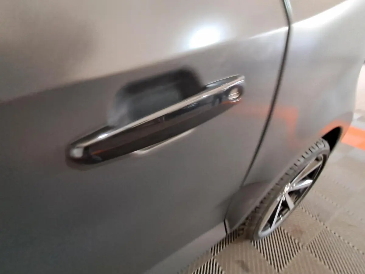 Gros plan sur la poignée de porte côté gauche d’une Aixam Ambition gris clair avec jante alliage noire diamantée visible.