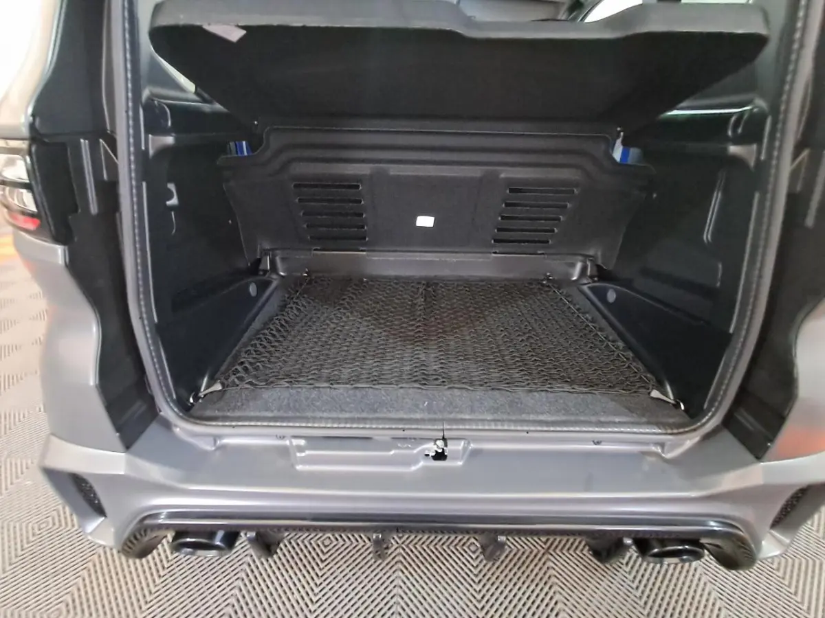 Coffre ouvert vu de l'arrière d'une Aixam Ambition gris clair, avec filet de rangement et pare-chocs sport visible.