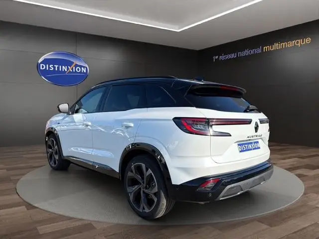 Vue 3/4 arrière d’un Renault Austral blanc nacré avec toit noir et hayon motorisé dans un showroom.