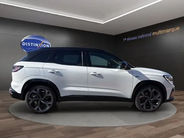 Vue de profil côté gauche du Renault Austral blanc nacré avec toit noir et jantes noires dans un showroom.