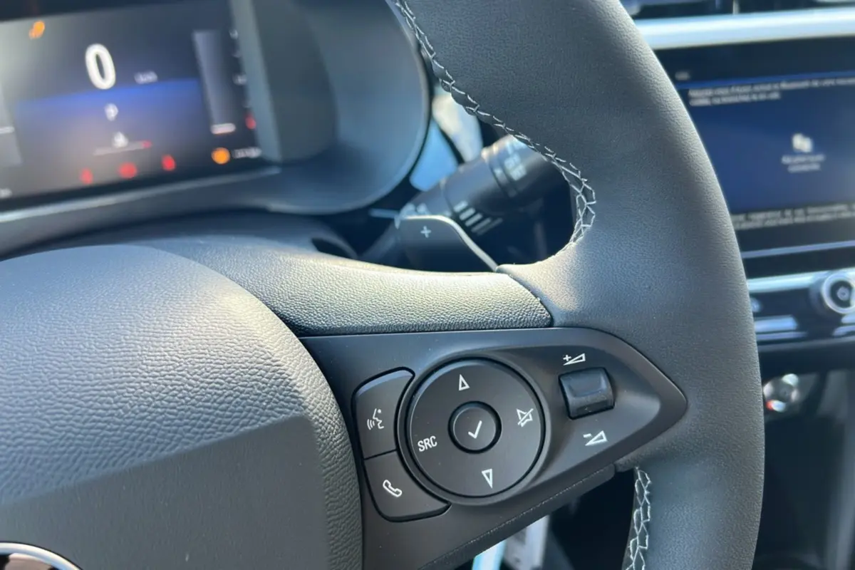 Gros plan sur le volant cuir noir de l’Opel Corsa Hybrid 2026 avec commandes multifonctions et affichage numérique en arrière-plan.