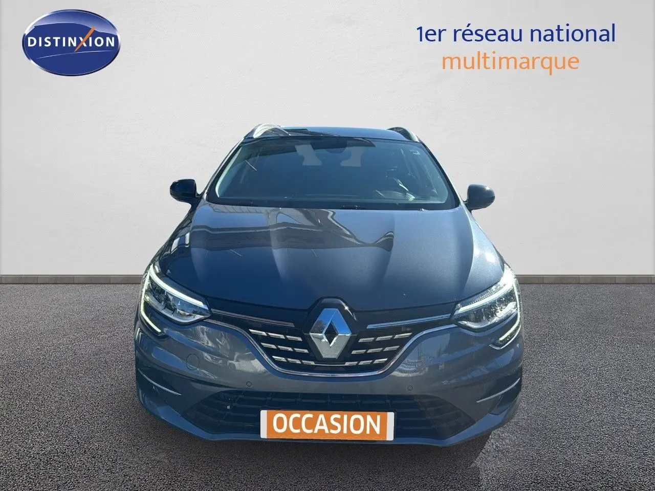 Vue avant d'une Renault Mégane Break gris titanium métal 2024 avec calandre et phares LED allumés.