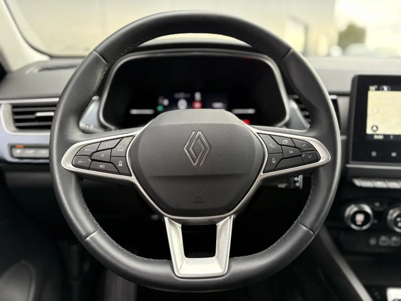 Vue rapprochée du volant en cuir noir avec commandes intégrées du Renault Arkana 2025, intérieur moderne et écran tactile visible.
