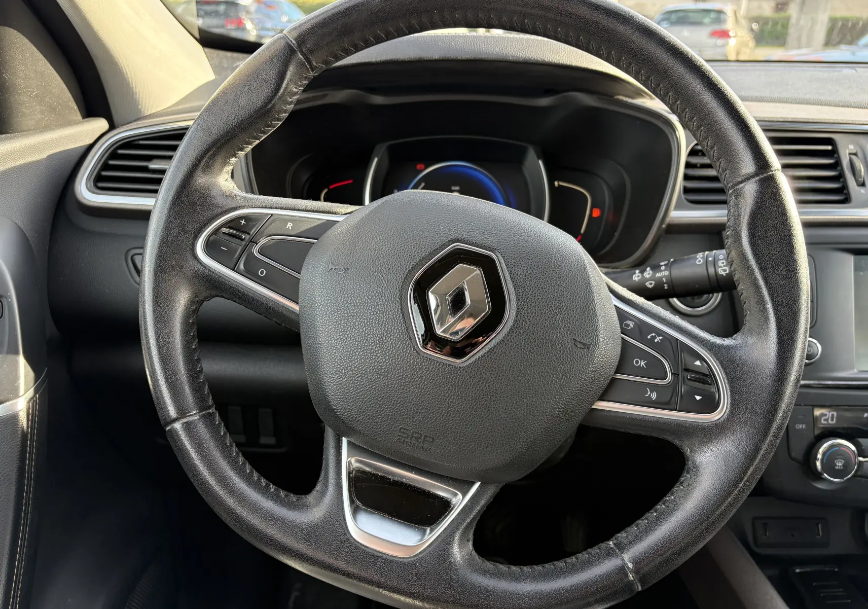 Gros plan sur le volant en cuir noir avec logo Renault, tableau de bord et commandes visibles dans un Renault Kadjar 2015.