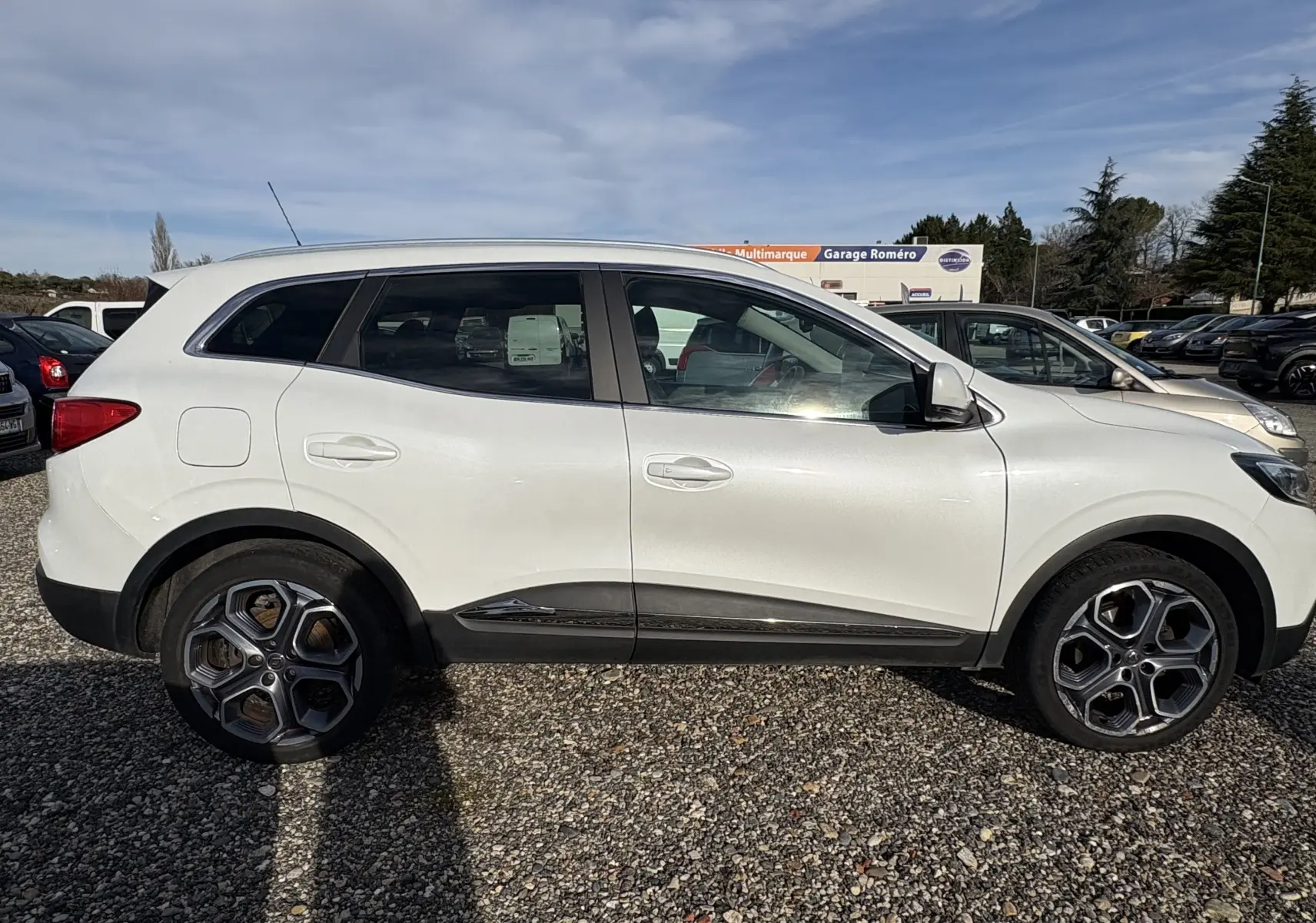 Profil côté gauche d’un Renault Kadjar blanc de 2015 avec jantes alliage et détails noirs sur les bas de caisse.