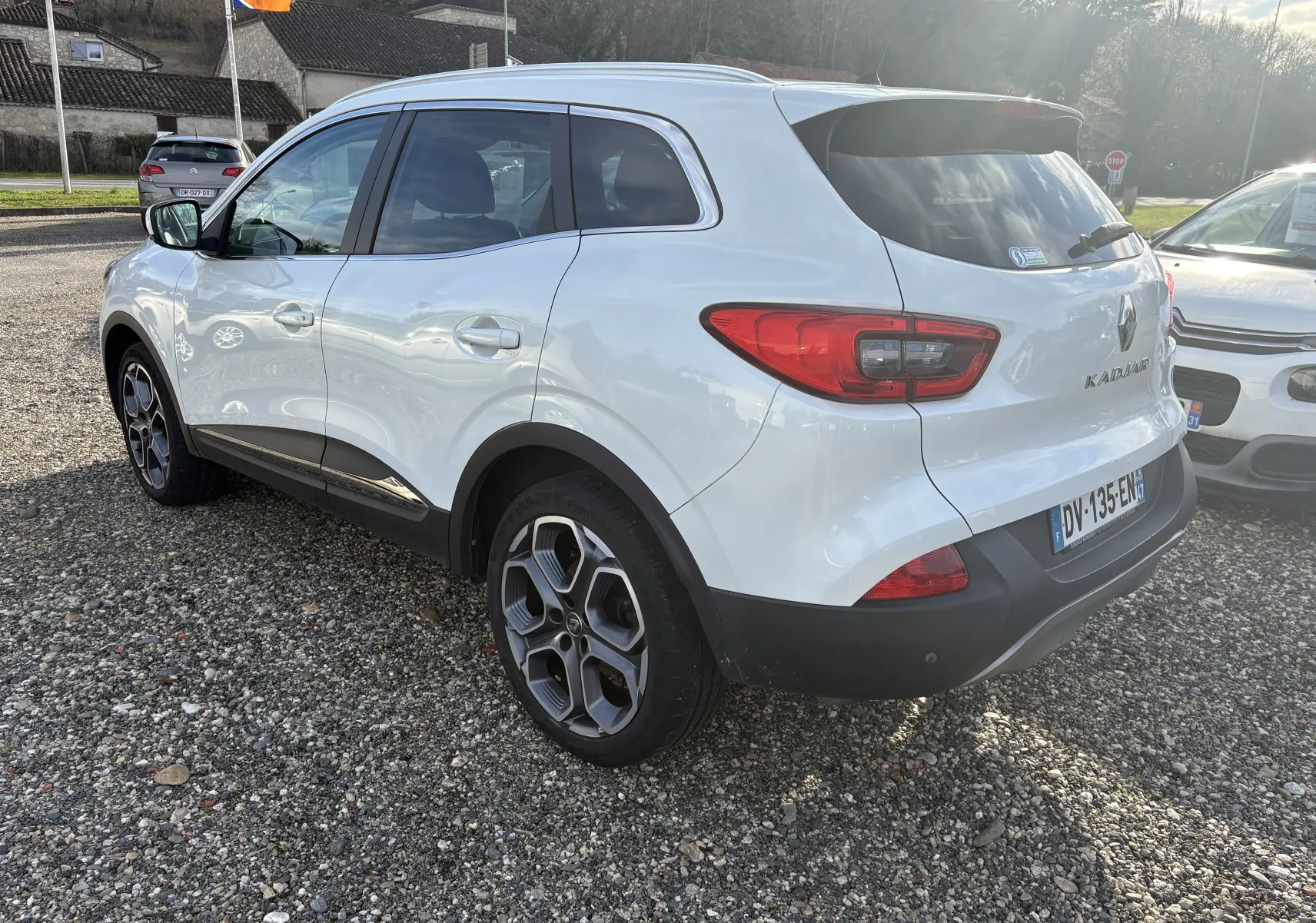 Renault Kadjar blanc vu en 3/4 arrière droit, avec jantes alliage et feux arrière distinctifs, stationné sur gravier.