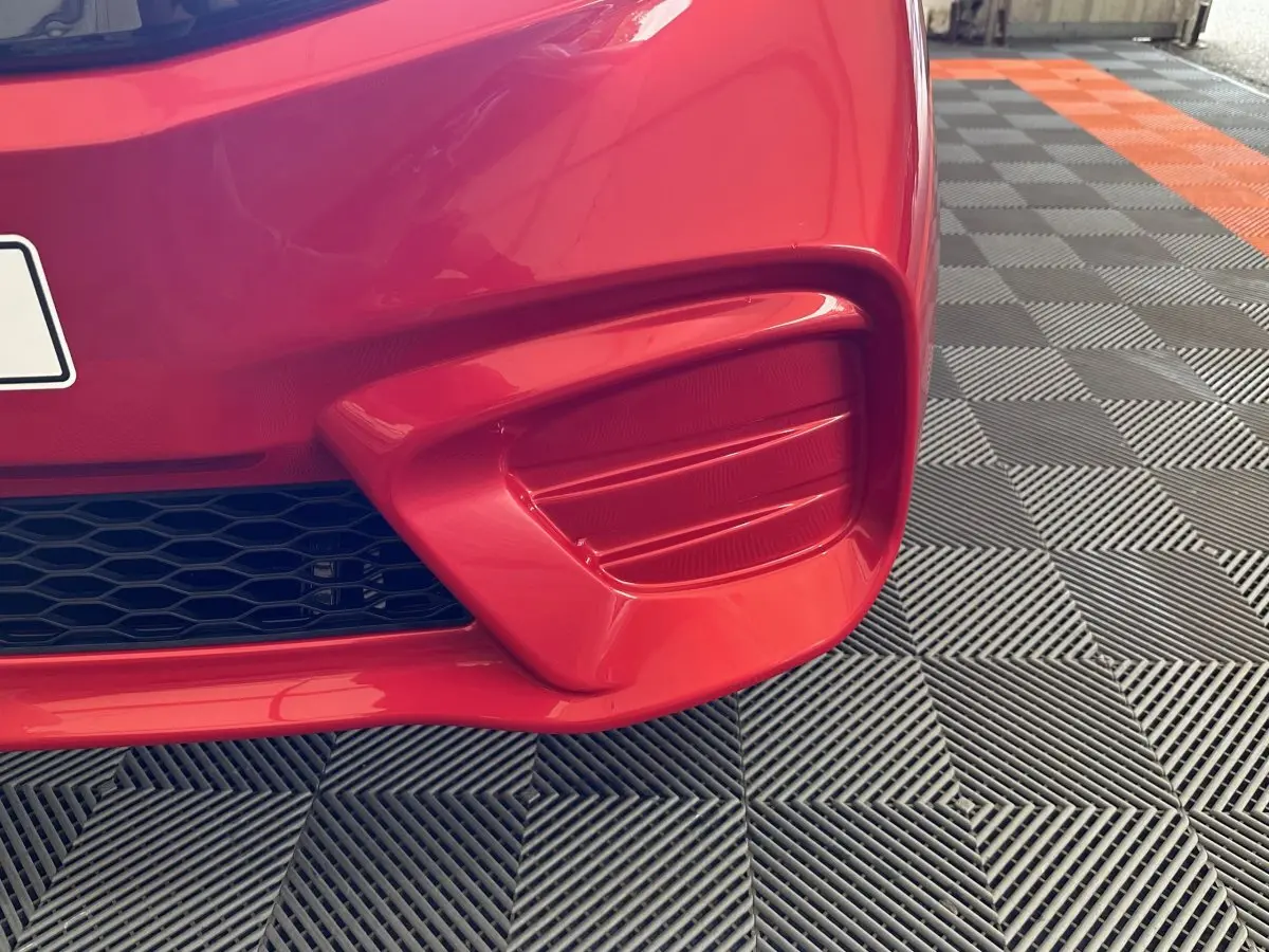 Gros plan sur le pare-chocs avant droit rouge de l'AIXAM AMBITION E CITY PACK 2026 avec grille noire et lignes sculptées.