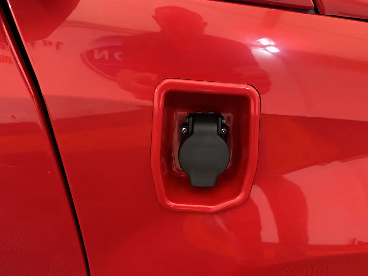 Prise de recharge électrique en gros plan sur le côté gauche rouge de l'AIXAM AMBITION E CITY PACK 2026.