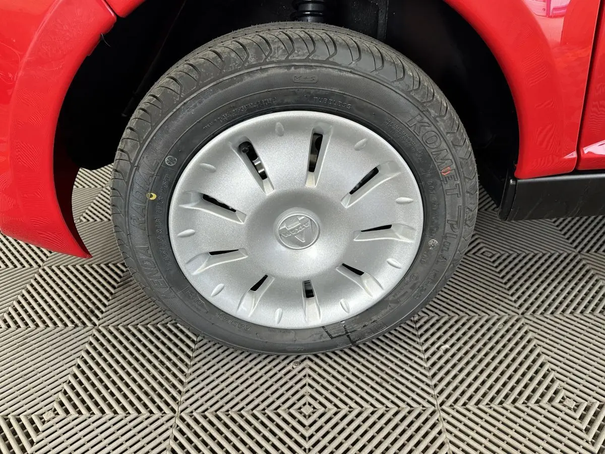 Gros plan sur la roue avant gauche d'une Aixam Ambition E City Pack rouge, avec jante argentée et pneu Komet Plus.