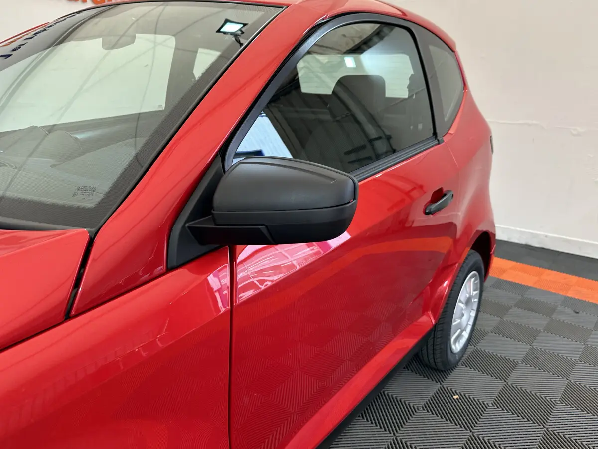 Vue de côté droit rapprochée sur l'AIXAM AMBITION E CITY PACK rouge avec rétroviseur caméra côté conducteur visible.