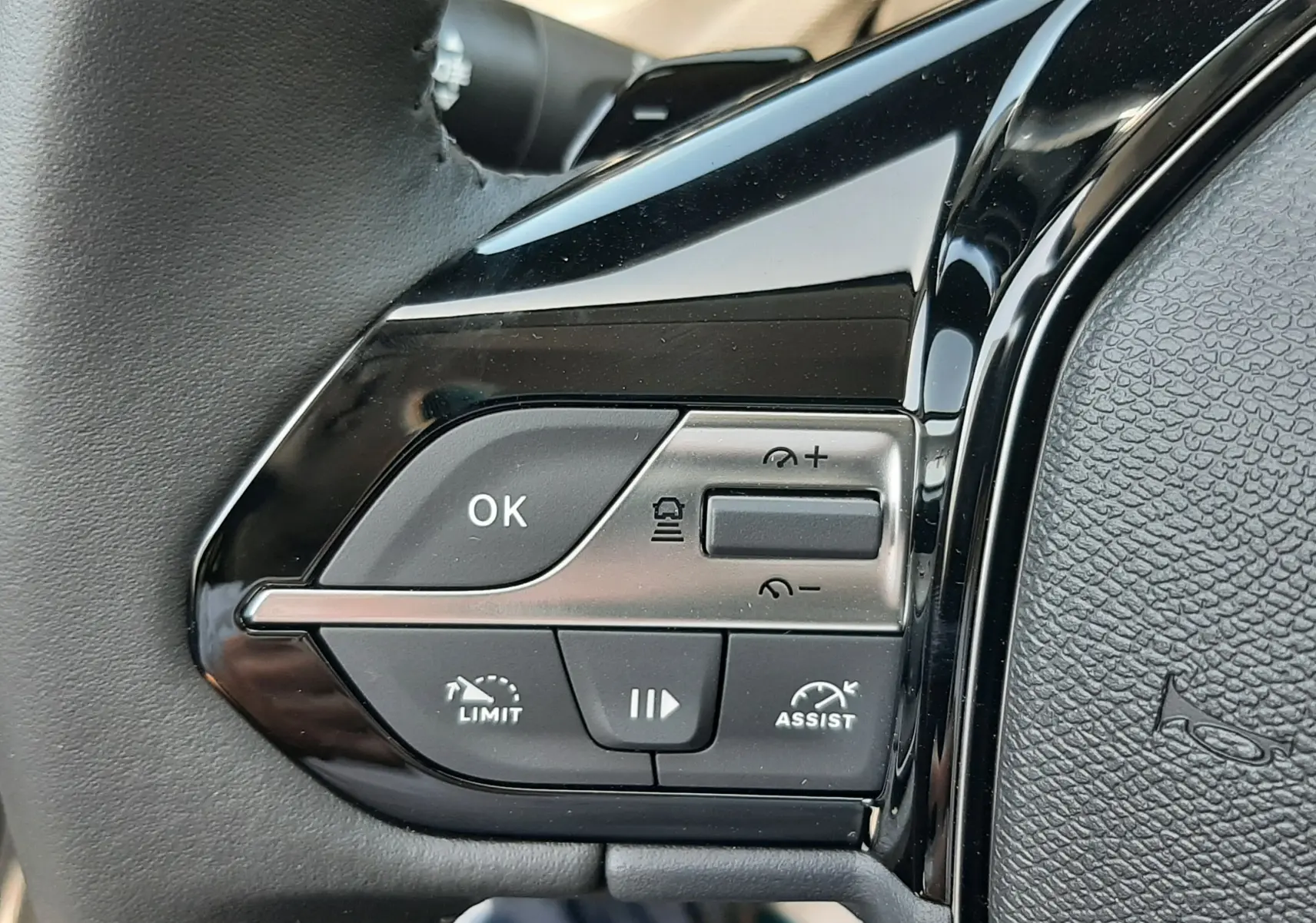Gros plan sur les commandes noires du volant côté gauche du Peugeot 308 gris sélénium, boutons multifonctions visibles.