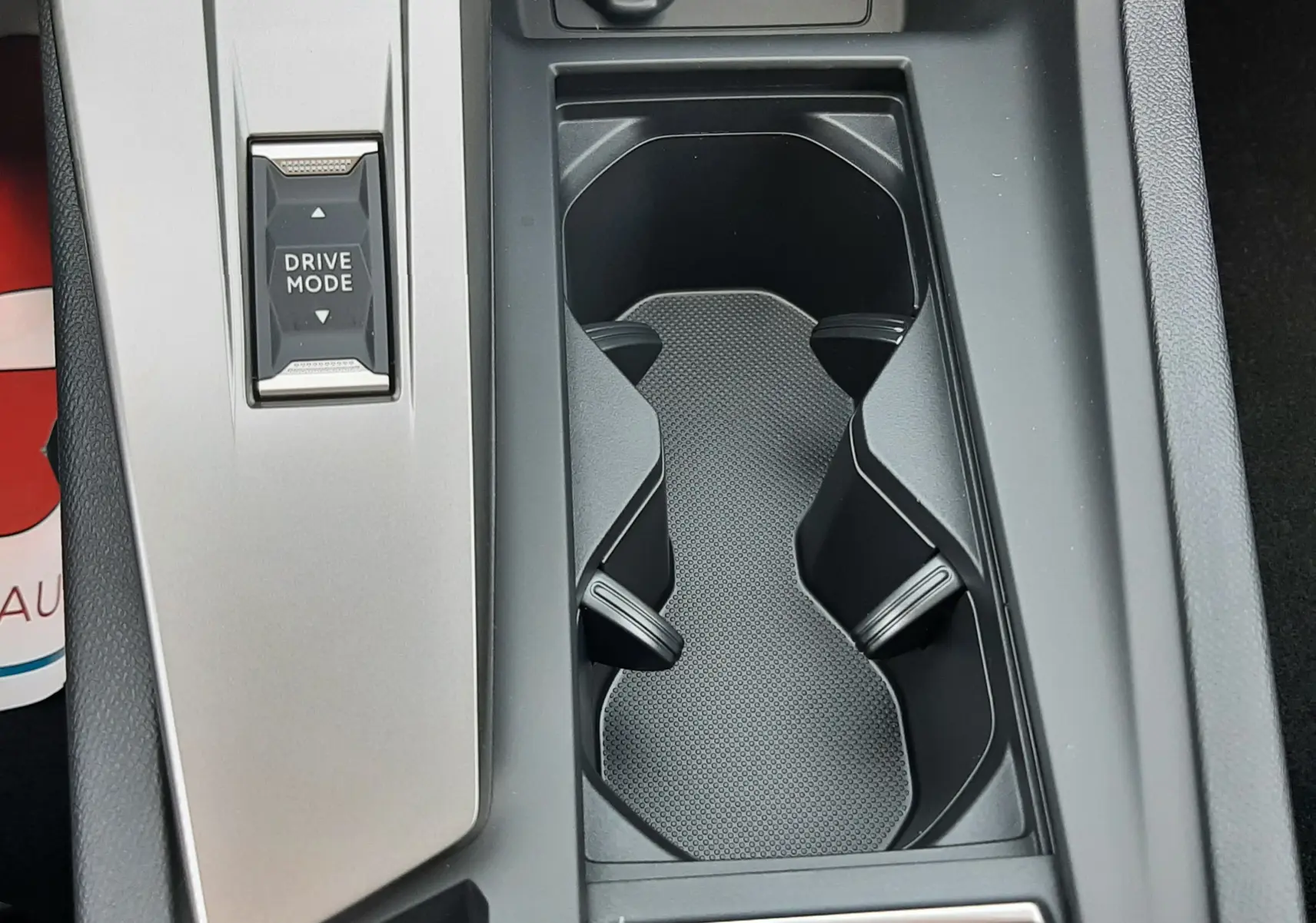 Vue en plongée du porte-gobelets central et du bouton Drive Mode de la console intérieure grise du Peugeot 308 III Ph.2.
