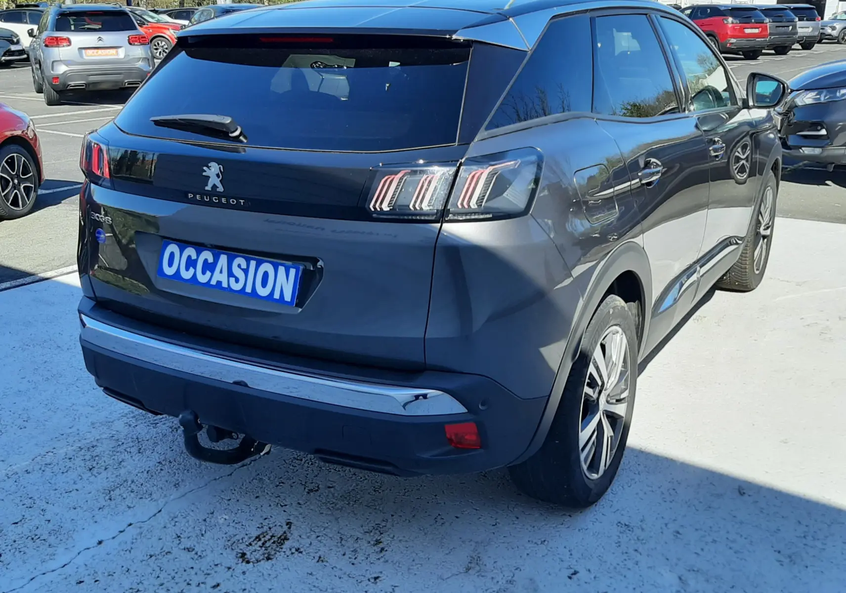 Vue 3/4 arrière droite d'un Peugeot 3008 gris platinium avec feux arrière à LED et attelage visible en parking.