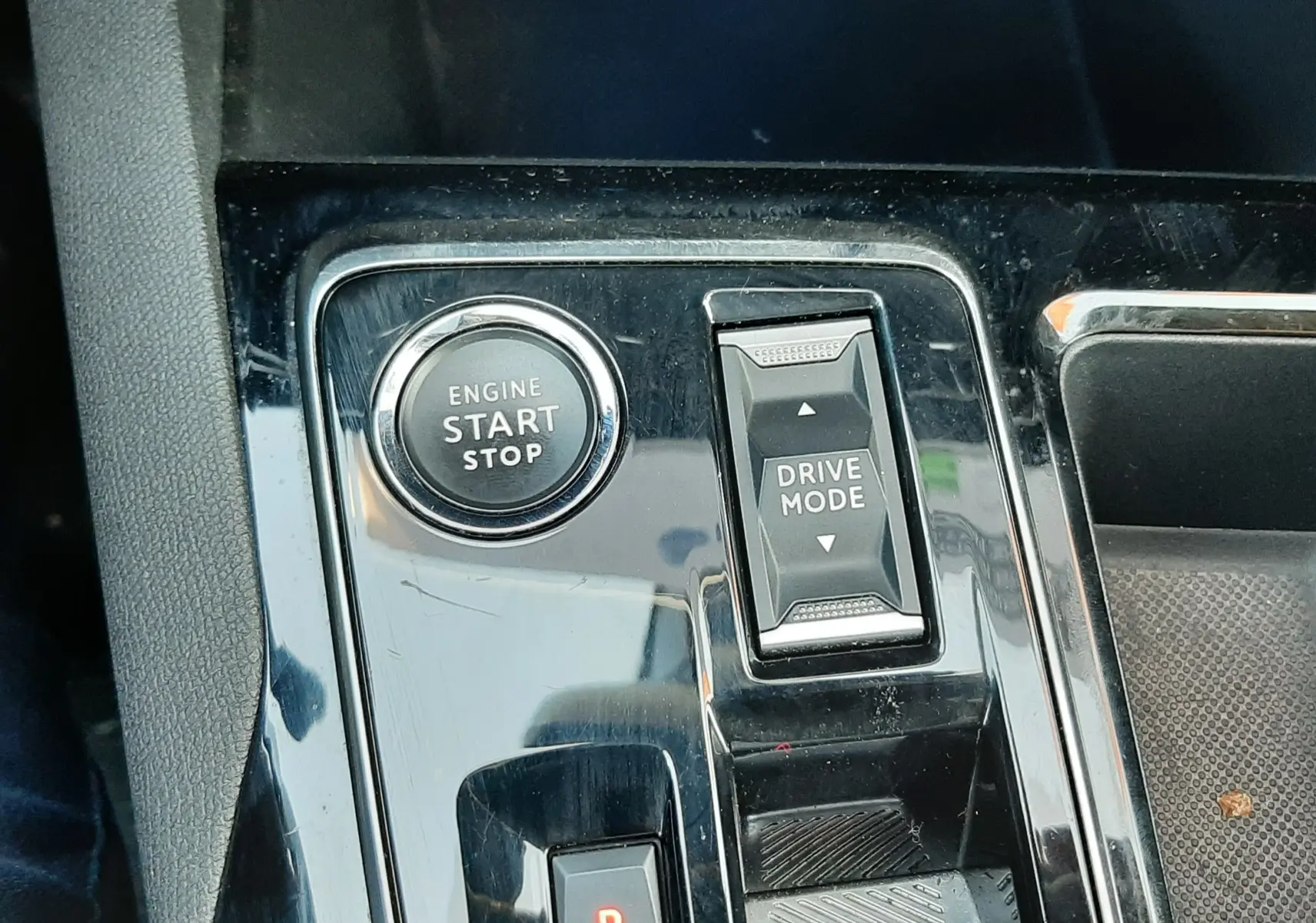 Gros plan sur la console centrale noire brillante du Peugeot 3008 2023, avec bouton start/stop et sélecteur drive mode.