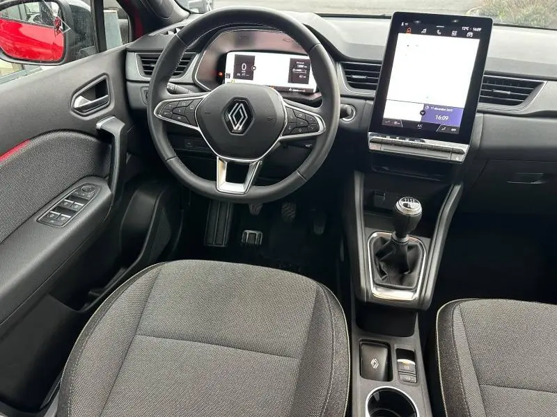 Vue intérieure frontale du Renault Captur 2025 avec volant, écran tactile vertical et levier de vitesses manuel, reflet rouge sur la portière.